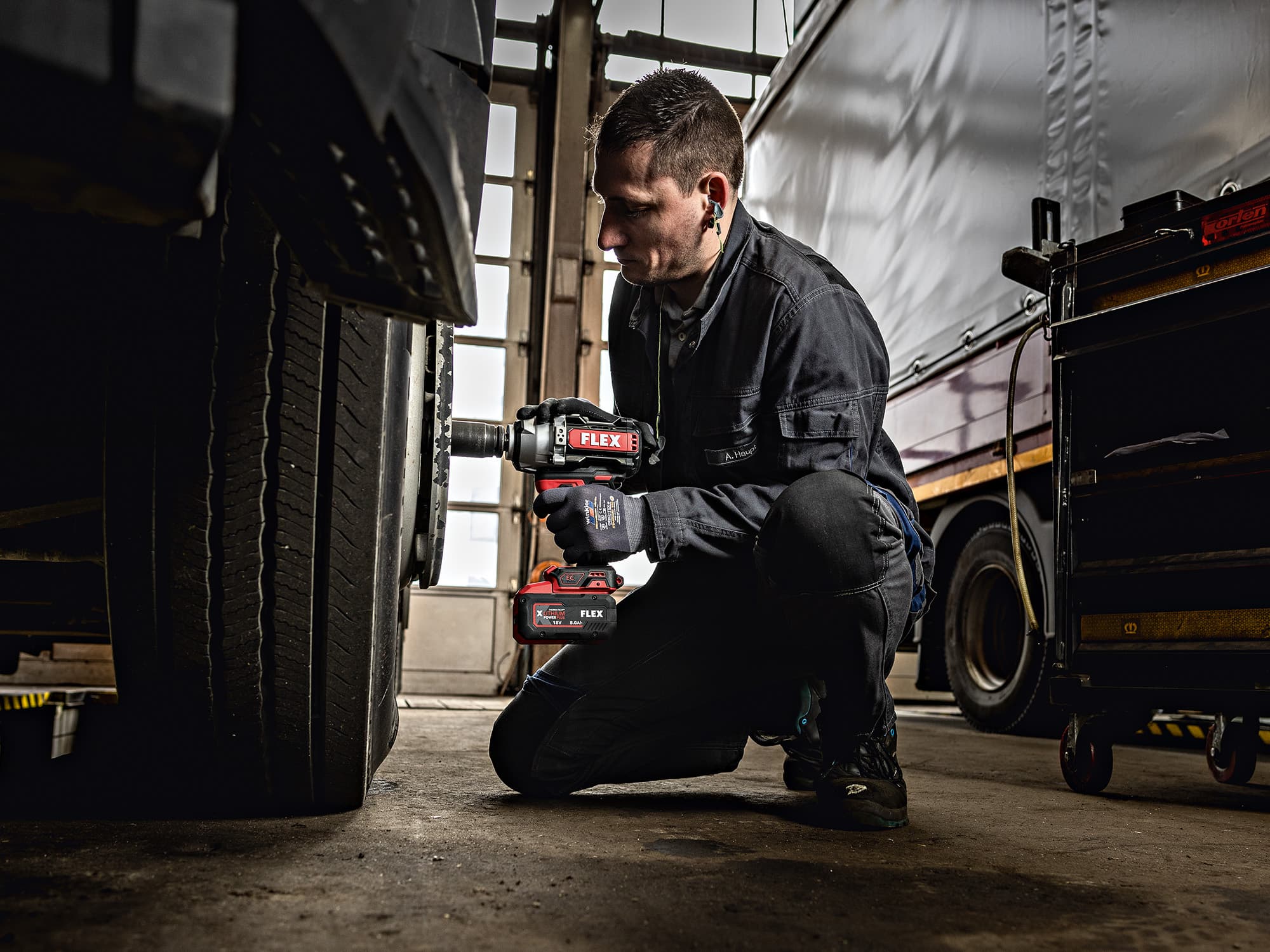 A mechanic tightens a screw on a truck tyre using a FLEX cordless impact wrench