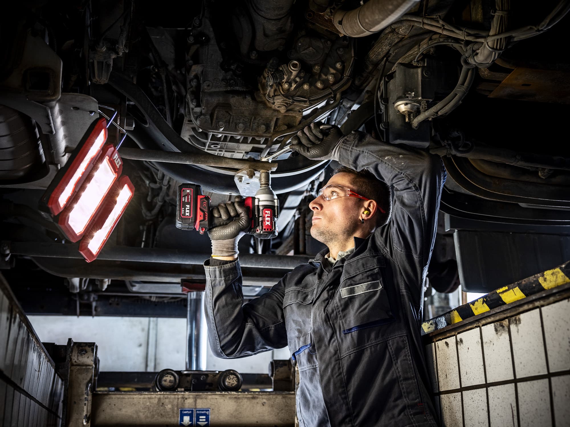 Car mechanic tightens screws underneath a vehicle