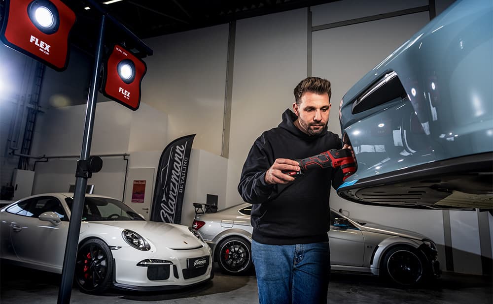 A blue car is being polished by a vehicle detailer using the FLEX PXE smart polisher.