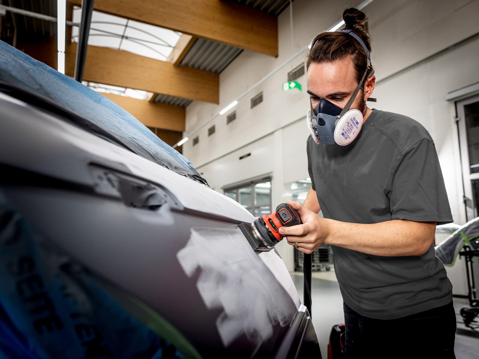 A bodywork mechanic sands paint on a car door using the orbital sander from FLEX.