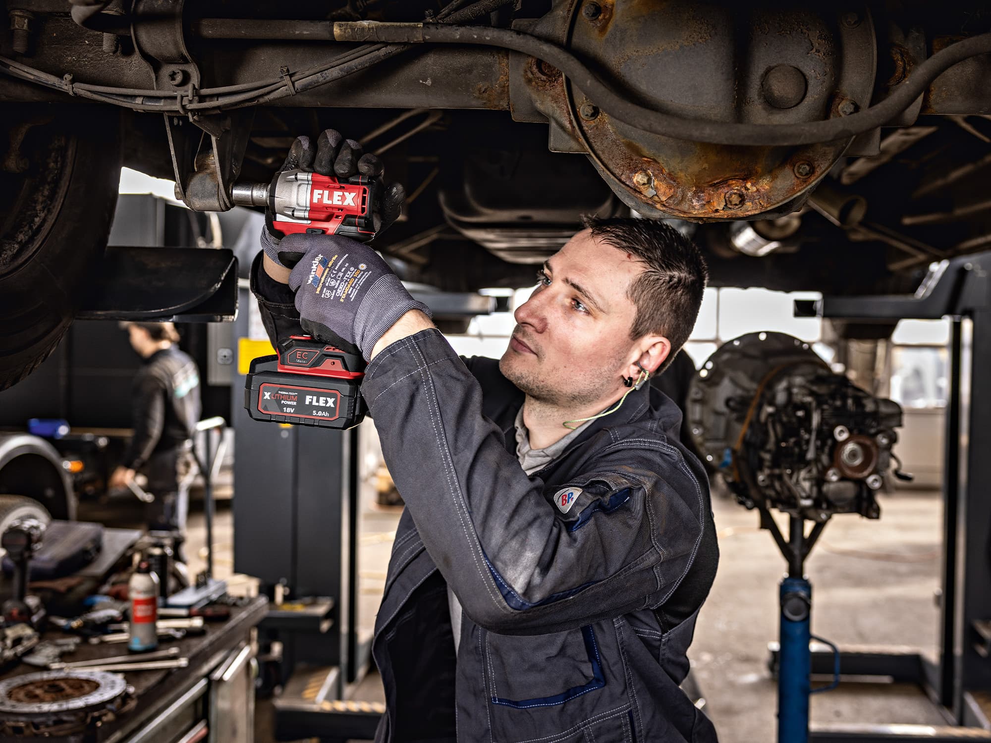 A car mechanic tightens screws on the body of a truck using a FLEX hammer drill.