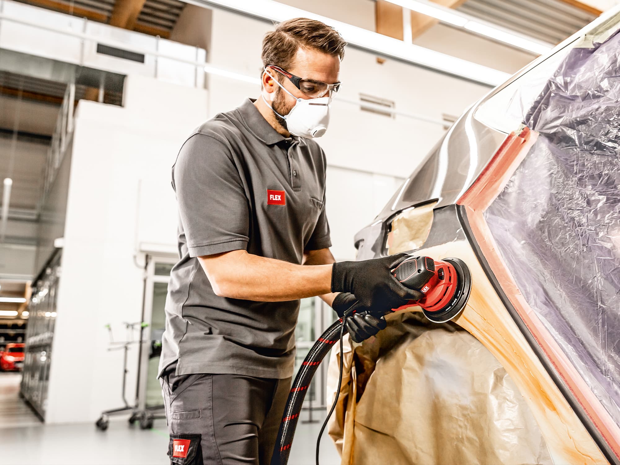 A bodywork mechanic sands paint on a car door using the eccentric sander from FLEX